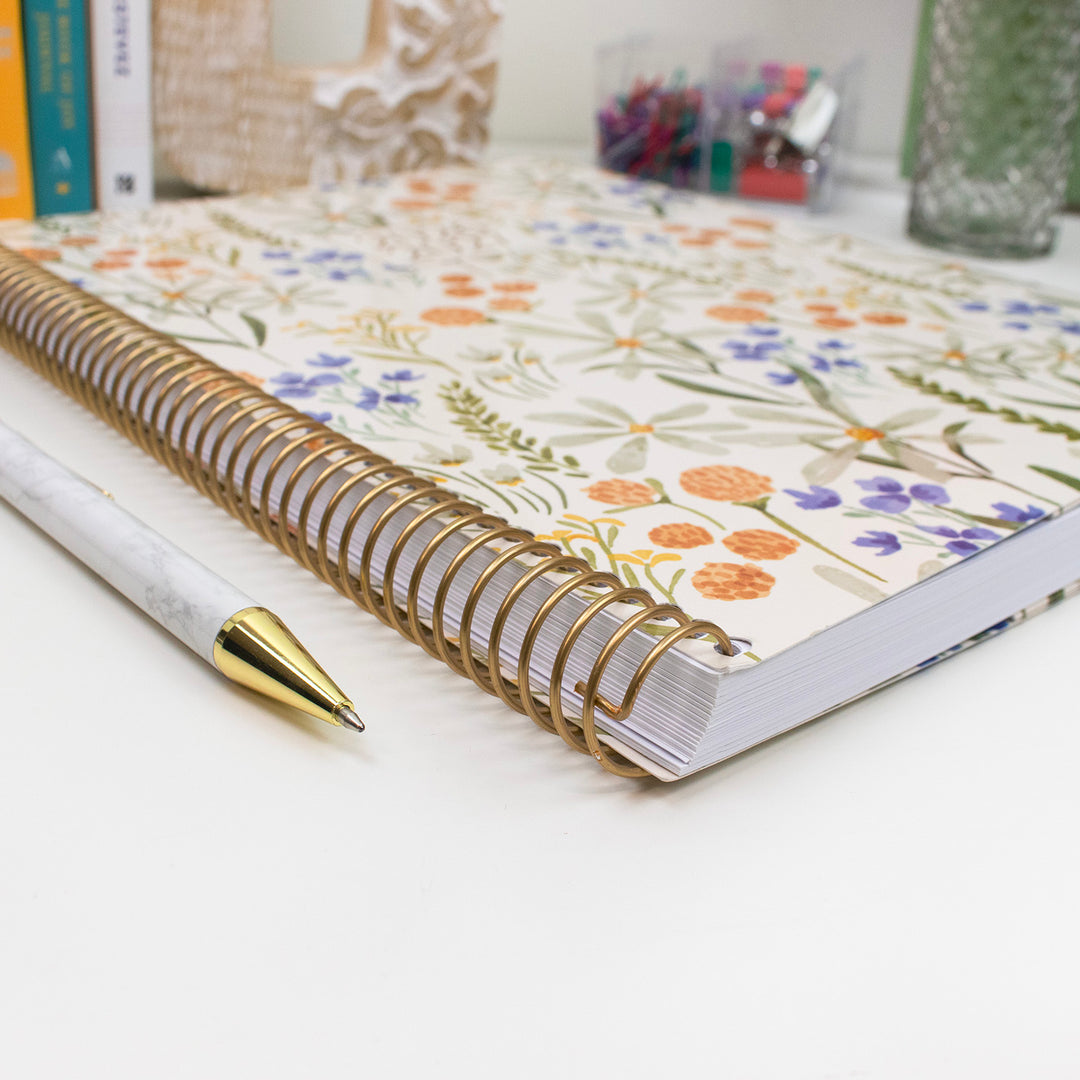 Planner with premium gold metal binding. A floral design and a pen on a white surface