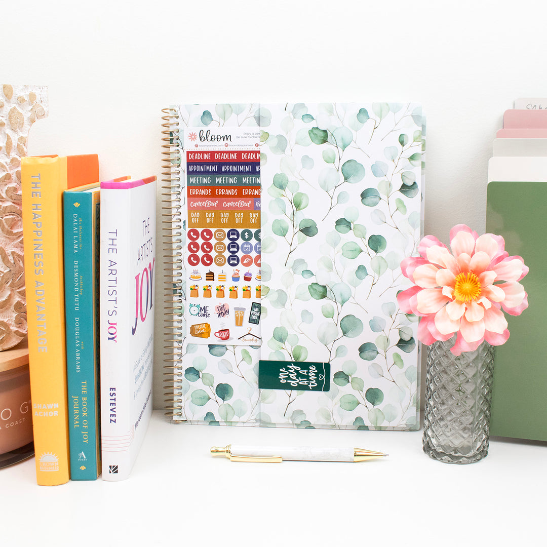 Decorative planner with floral design, books, and a flower on a white surface