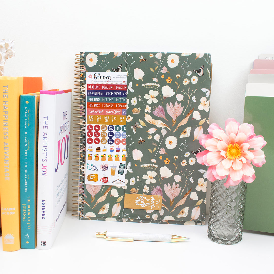 Floral planner with stickers and a pink flower in a vase on a white surface