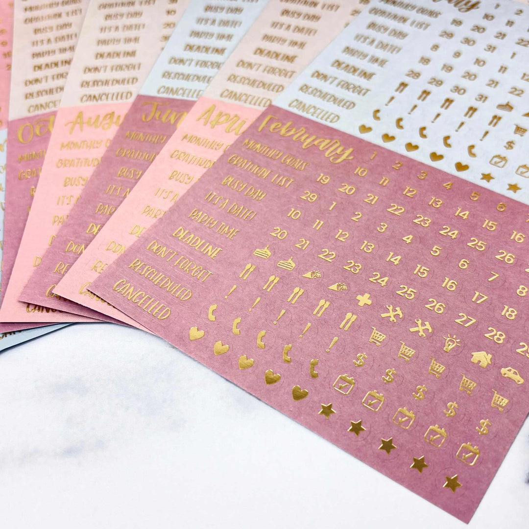 Pink stickers with gold text and symbols on a white surface