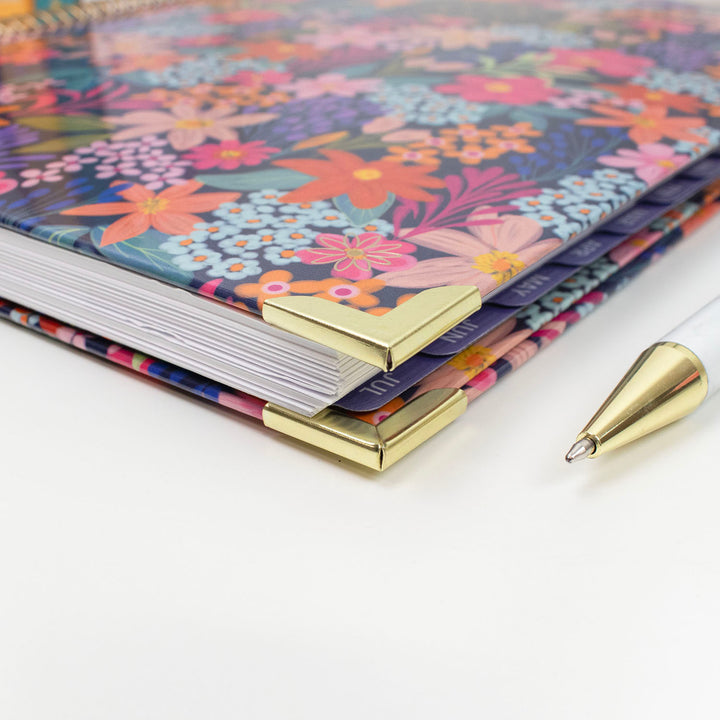 Stack of floral planners with a gold pen on a white surface
