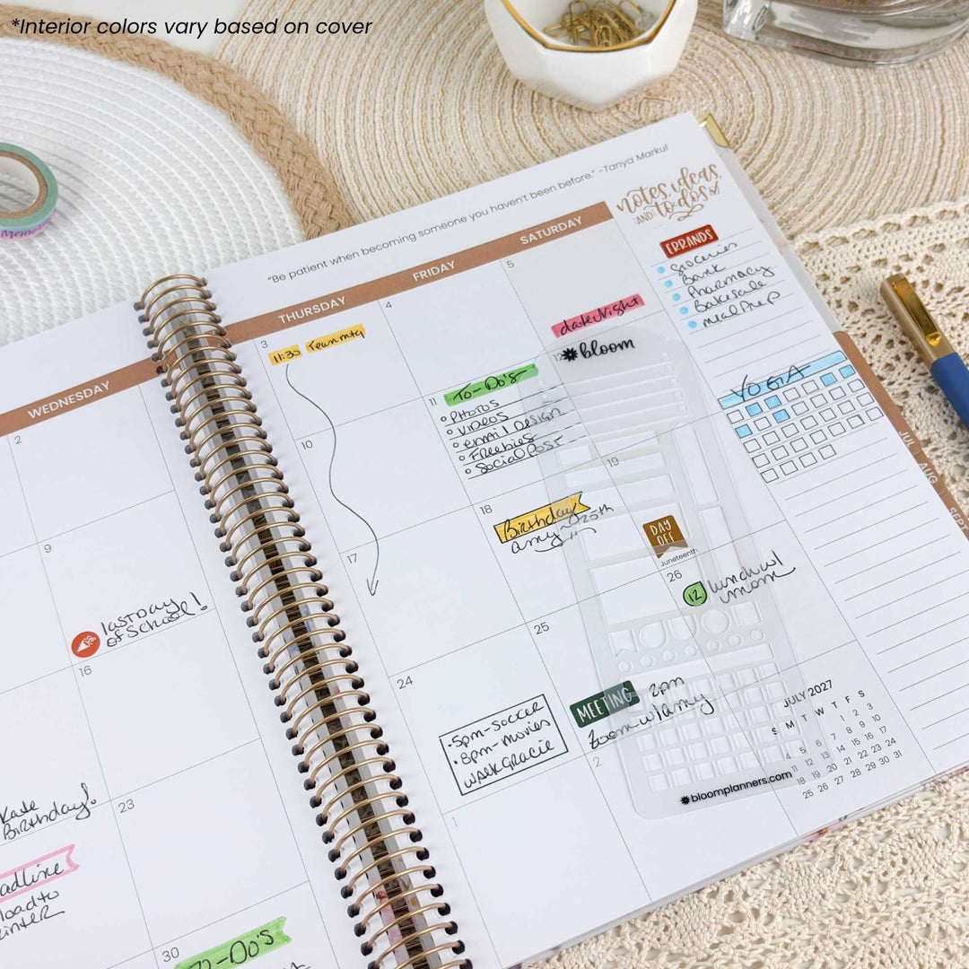An open spiral-bound planner showing a weekly calendar layout with lined pages, decorative stickers, and a clear date-cover insert. The planner is photographed on a woven beige table surface with a pen, dish, and other stationery items nearby.