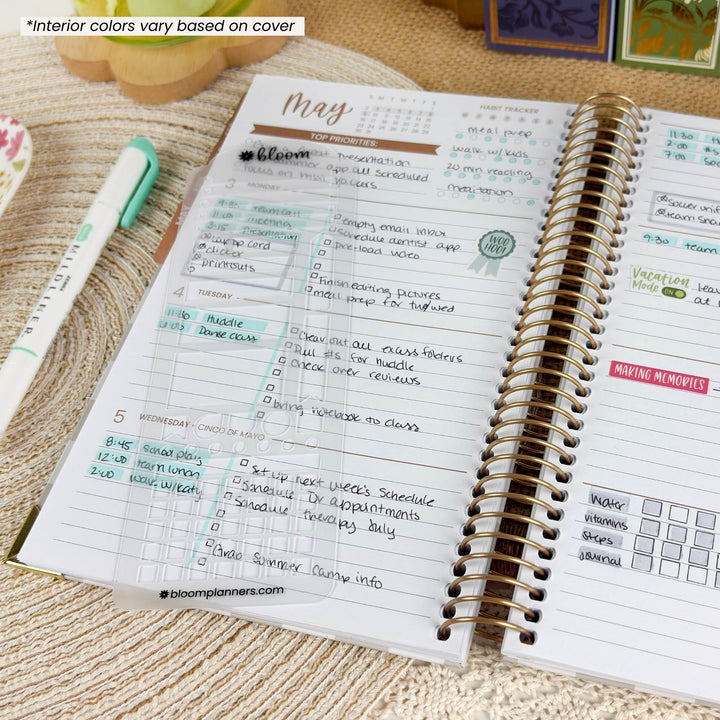 An open spiral-bound planner showing a handwritten monthly layout with pastel accents, photographed on a woven beige surface. A mint pen and part of another notebook are visible nearby.