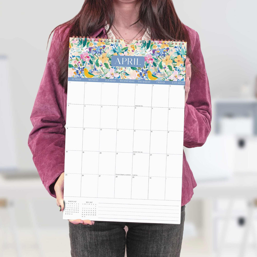 Person holding a floral-themed calendar pad with 'April' on it.