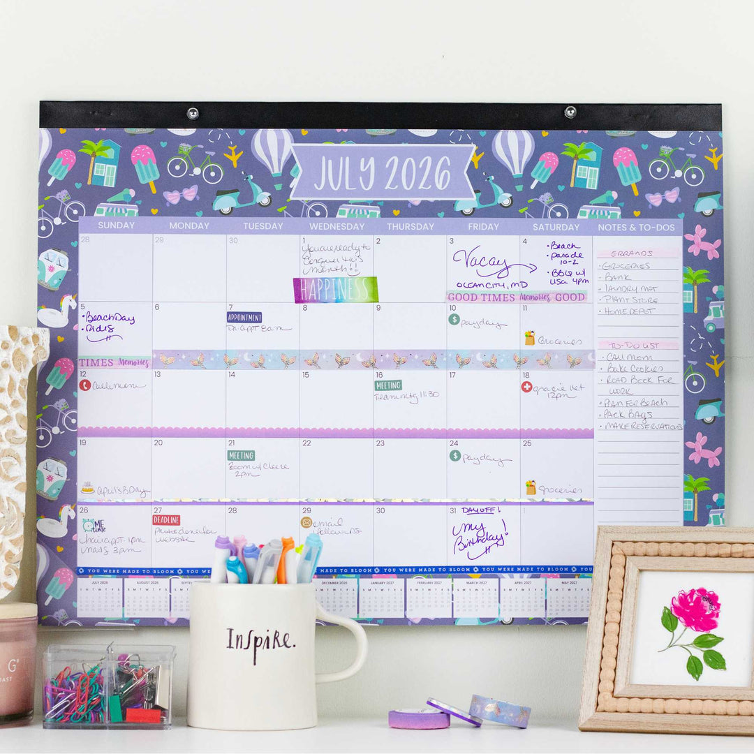 Colorful wall calendar for July 2026 on a desk with stationery items.