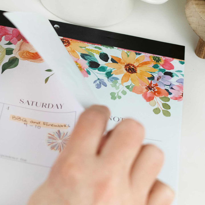 Hand holding a floral planner with a calendar on a white surface