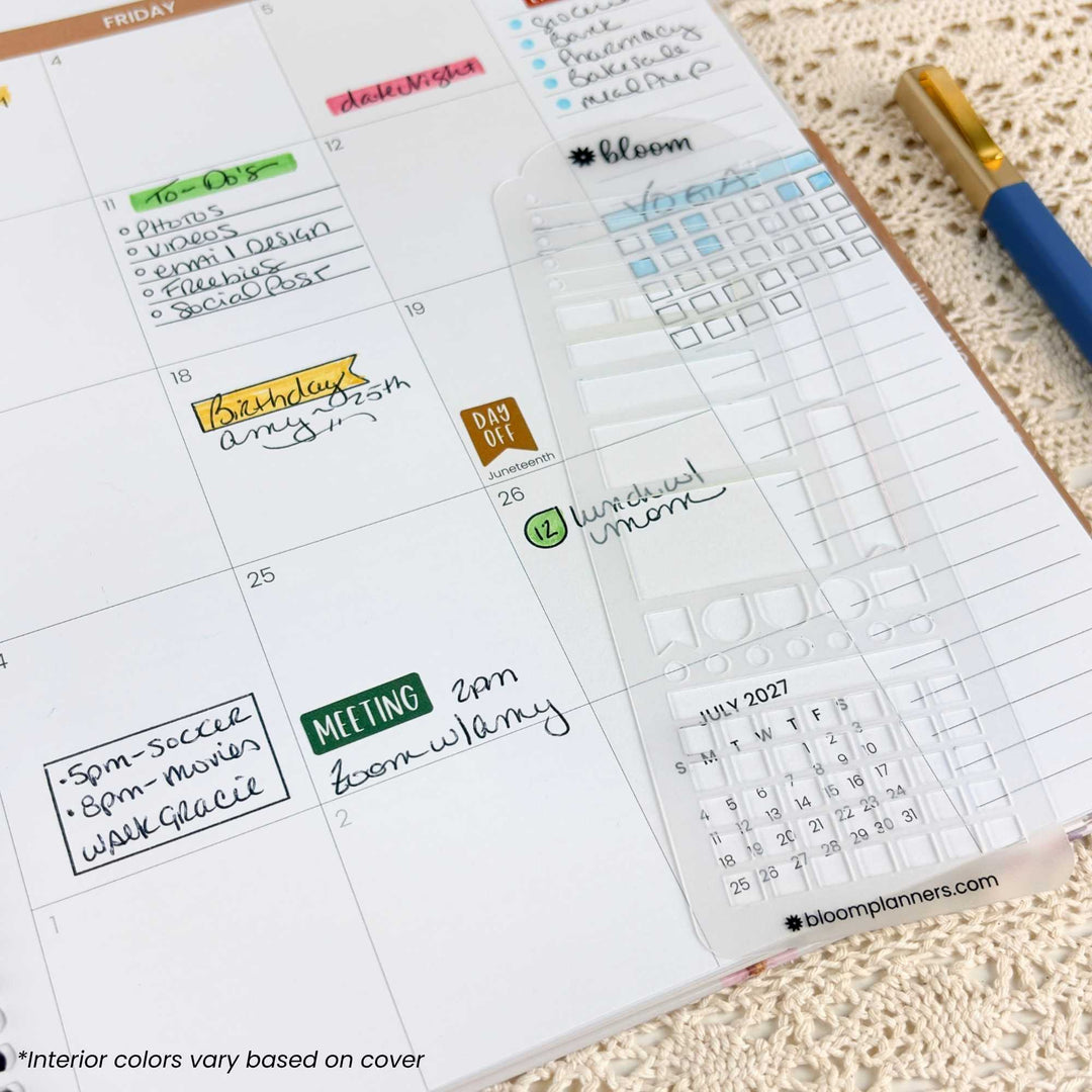 A close-up of a weekly planner page from a Bloom planner, showing handwritten notes, colored day labels, and a clear calendar sticker on a beige textured fabric background with a blue and gold pen nearby.