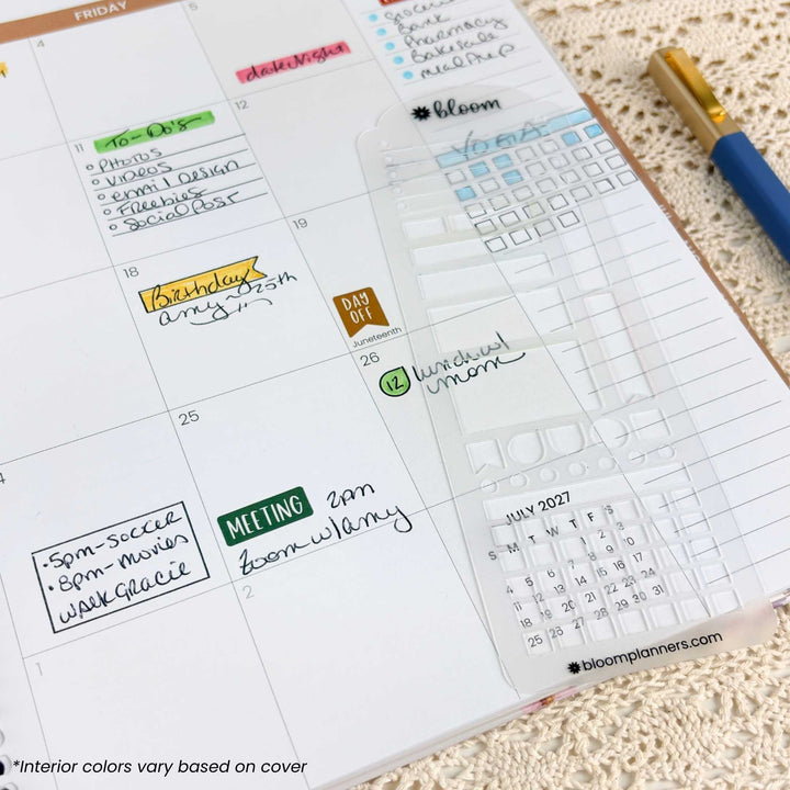 A close-up of a weekly planner page from a Bloom planner, showing handwritten notes, colored day labels, and a clear calendar sticker on a beige textured fabric background with a blue and gold pen nearby.