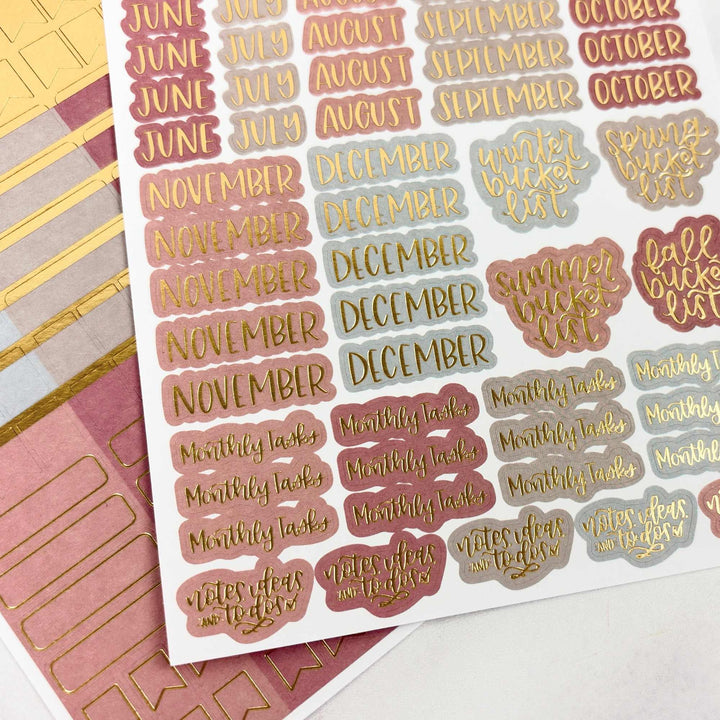 Sheet of planner stickers with months, seasons, and tasks on a pink and gold background.