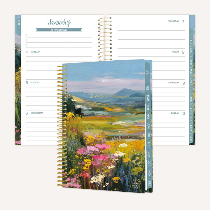 Spiral-bound planner with a scenic cover featuring mountains and flowers, open to a January page.