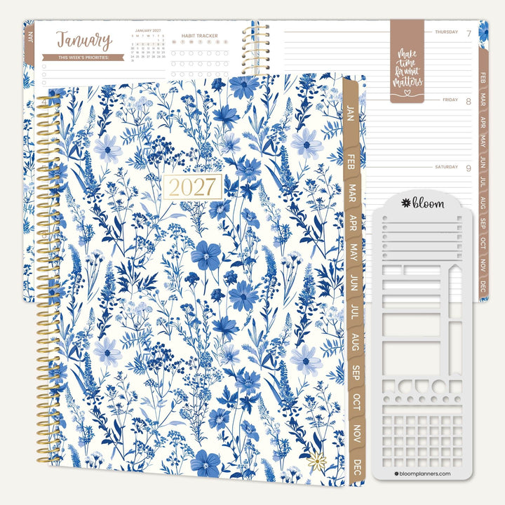 A 2027 spiral-bound planner shown open to the January page with floral inserts and a white planner sticker sheet on a light beige background. The cover features a blue and white floral pattern with gold-toned spiral binding and a small '2027' label.