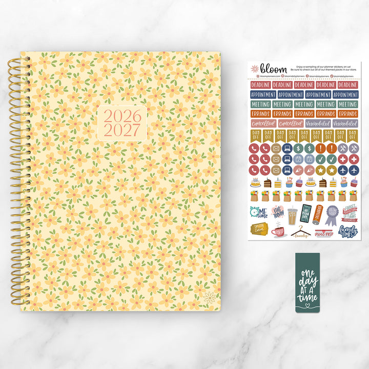 8.5" x 11" yellow floral planner, stickers, and a bookmark on a marble desk.
