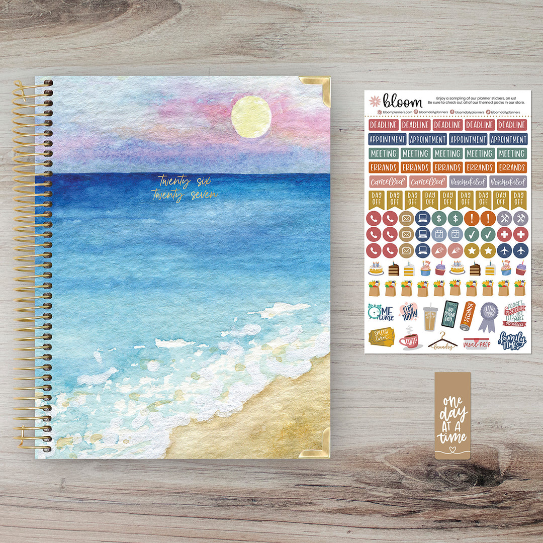 Planner with beach design cover and sticker sheet on a wooden surface