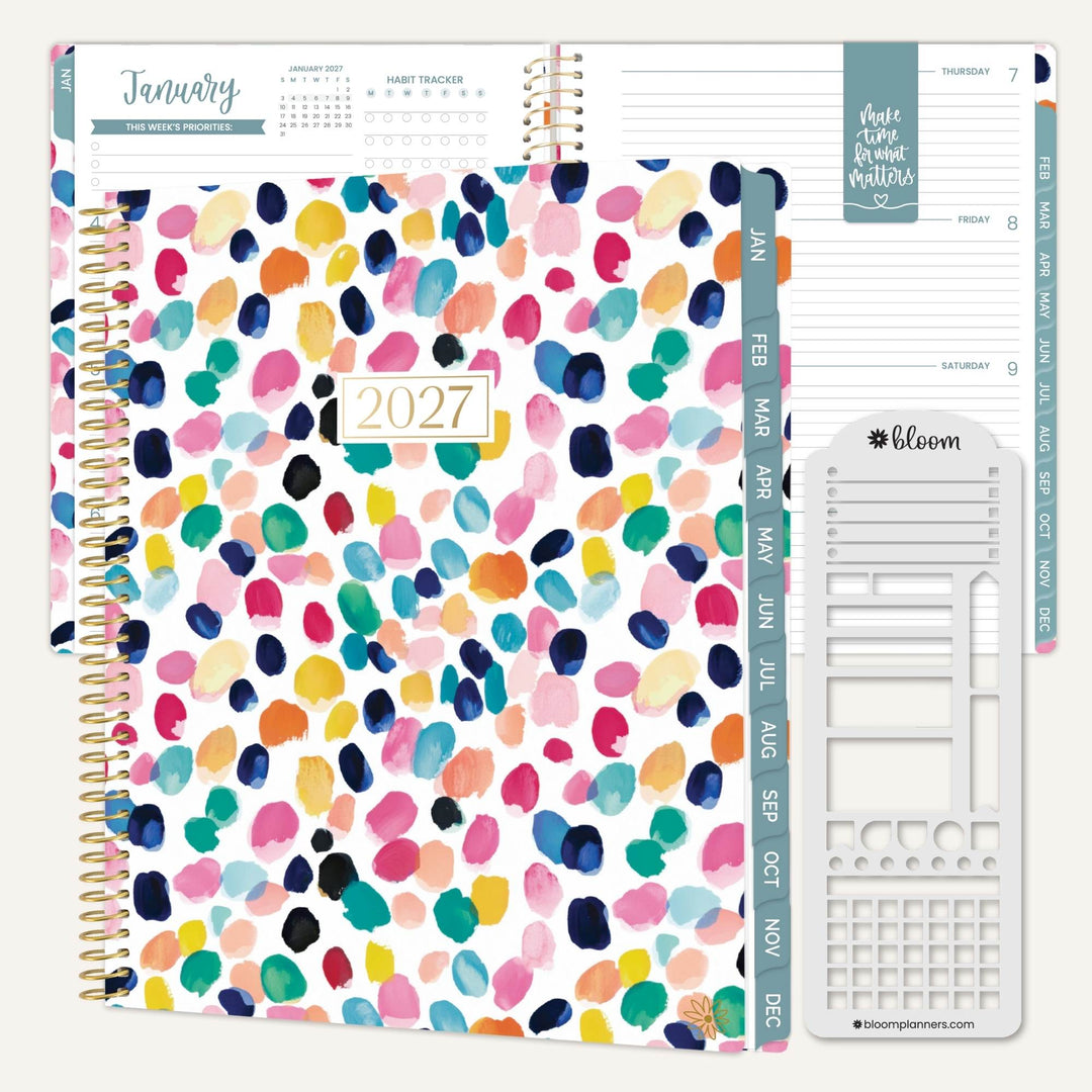 A 2027 monthly planner shown open with colorful watercolor paint-splatter covers, teal weekly tab strips, and a white monthly insert page on a clean white background.