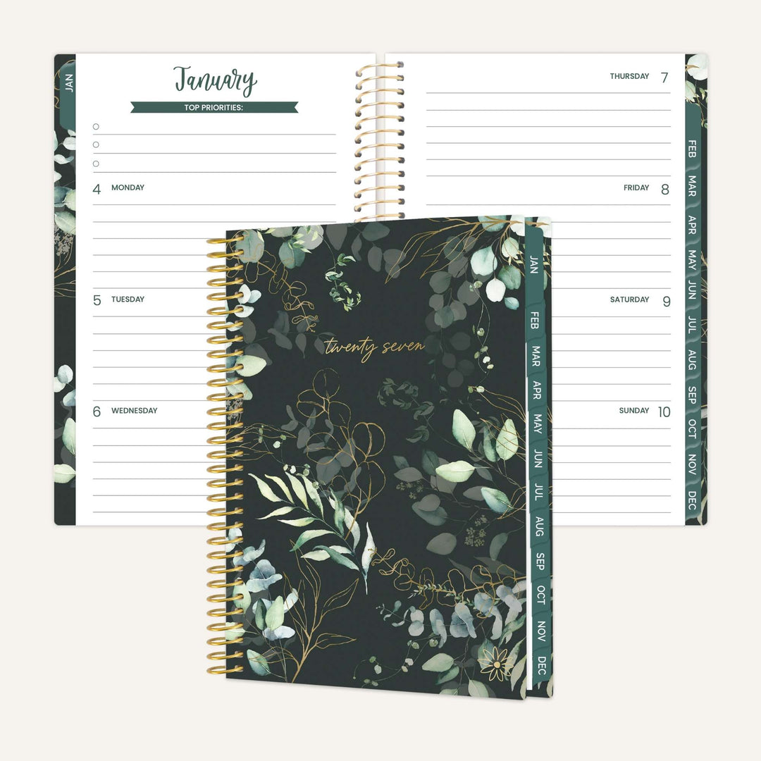 A spiral-bound planner shown open to January pages with a matching closed cover in front. The cover has a dark green and black botanical pattern with gold script reading 'twenty seven.