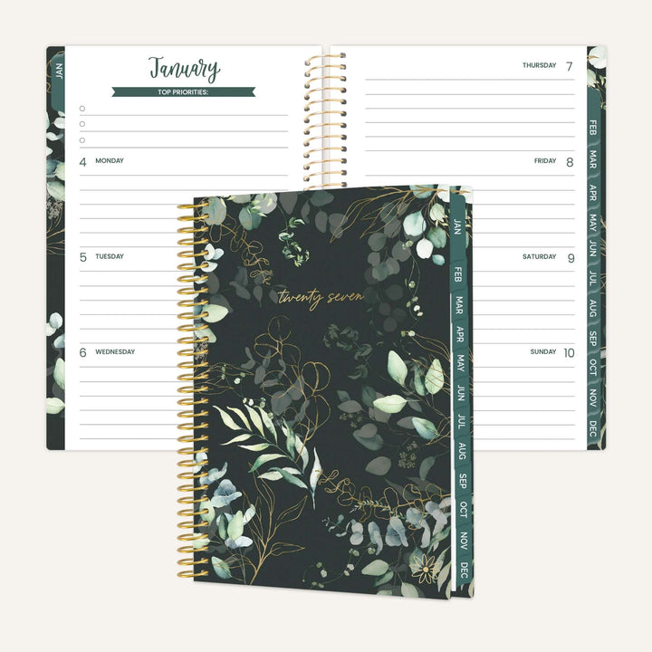 A spiral-bound planner shown open to January pages with a matching closed cover in front. The cover has a dark green and black botanical pattern with gold script reading 'twenty seven.
