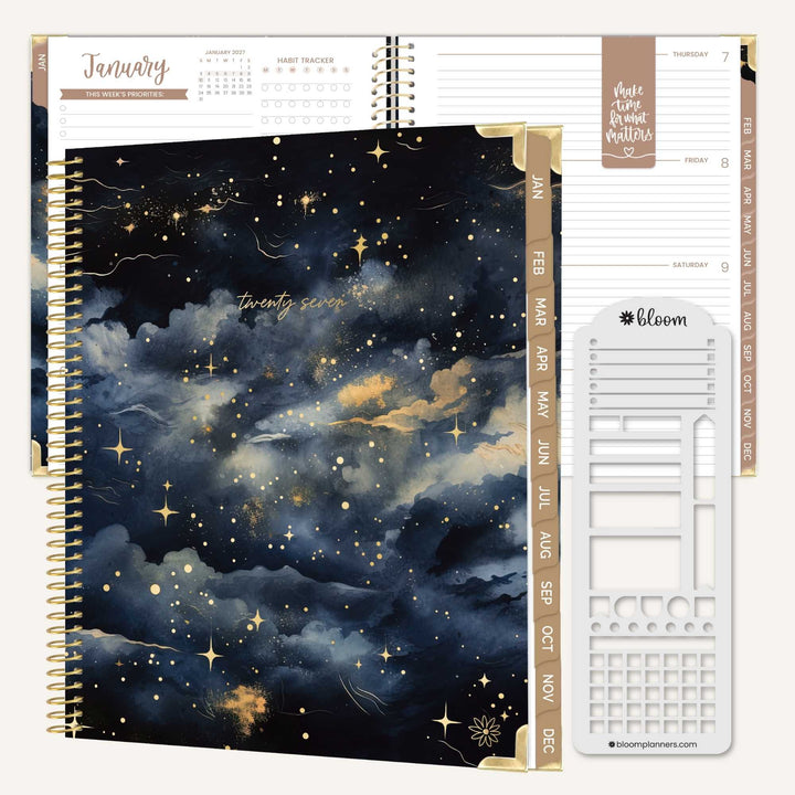 A spiral-bound planner shown open to a decorated cover page with a dark blue and black cloudy night sky and gold stars. The planner pages and inserts are visible behind it, including a January calendar page, weekly layout pages, and a white paperclip-shaped insert with the Bloom logo.