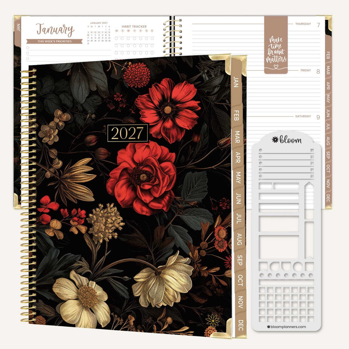 A 2027 spiral-bound planner shown open to display the interior layout, featuring a dark floral cover with red and cream flowers, gold-toned binding, monthly tabs, and a white sticker sheet labeled Bloom.
