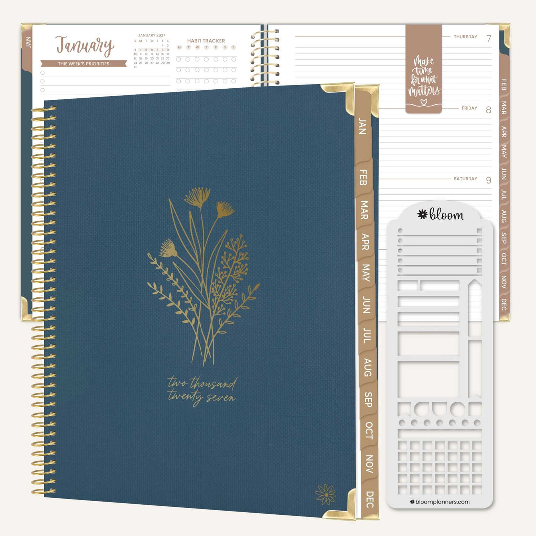 A spiral-bound planner shown open to a January page, with a navy blue cover featuring gold wildflower artwork and gold page headers. The planner is photographed on a clean white background with a Bloom brand sticker visible on the right.