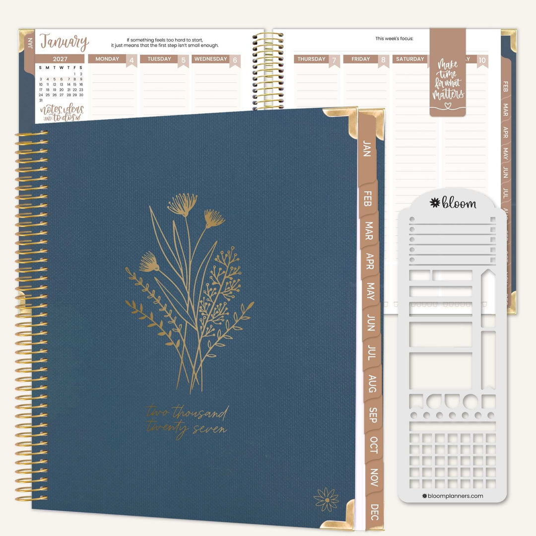 A navy blue spiral-bound planner shown open with interior pages, gold floral line art on the cover, gold page headers, and a white sticker sheet labeled bloom placed to the right. The product is photographed on a clean white background.