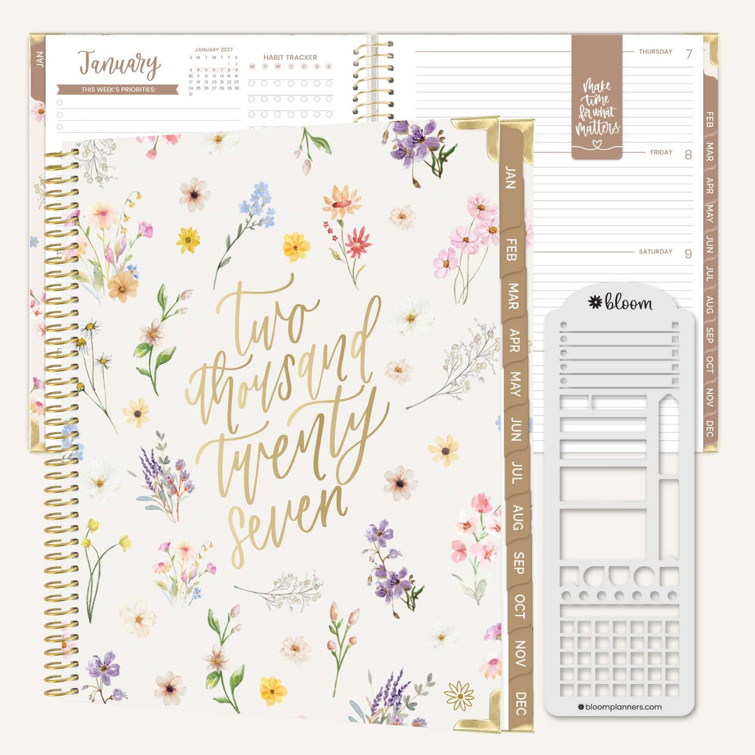 A floral planner shown open with interior pages and a white sticker sheet. The cover has gold script reading 'Two thousand twenty seven' and a watercolor flower pattern in soft pink, purple, yellow, and blue tones.