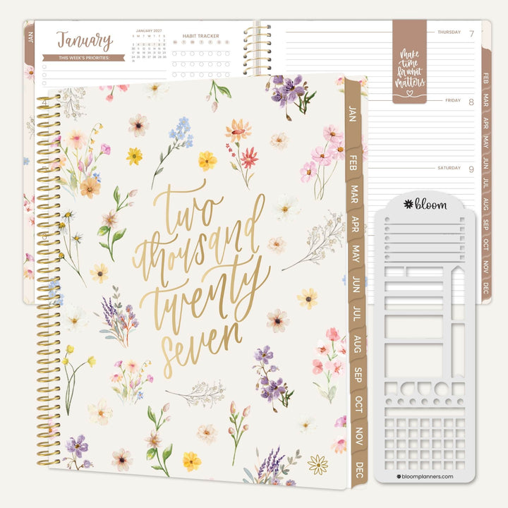 A spiral-bound planner shown open to multiple pages, featuring a cream floral cover with gold script reading 'two thousand twenty seven.' The planner includes tan monthly tabs, lined writing pages, a calendar tracker, and a white sticker/decal sheet.