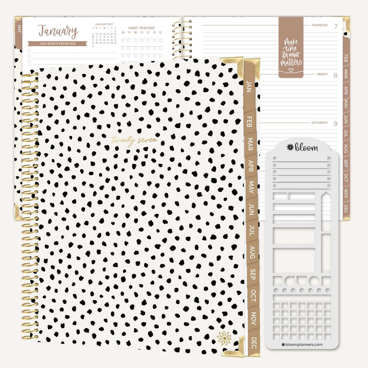 A spiral-bound planner set shown open on a white background, featuring a black-and-white polka dot cover, gold-toned binding and tabs, and white interior pages with planner inserts and a monthly calendar page.