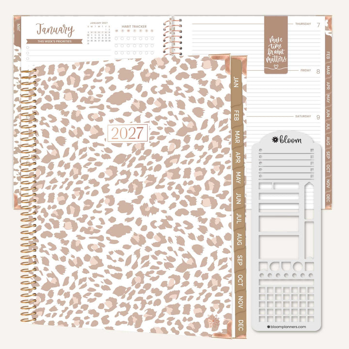 A 2027 spiral-bound planner shown open with interior pages, featuring a leopard print cover in beige and taupe tones, rose-gold-toned ring binder and page accents, and a sheet of white planner stickers on a light neutral background.