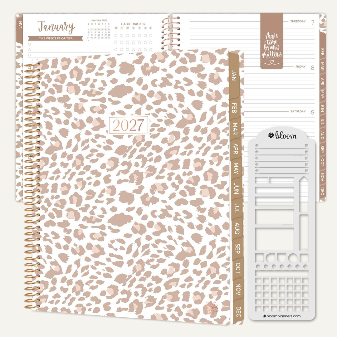 A spiral-bound 2027 planner shown open with interior pages and a white planner insert tool on a light beige background. The cover has a white base with a dusty rose leopard print, and the interior pages and tabs are in blush pink and taupe tones.