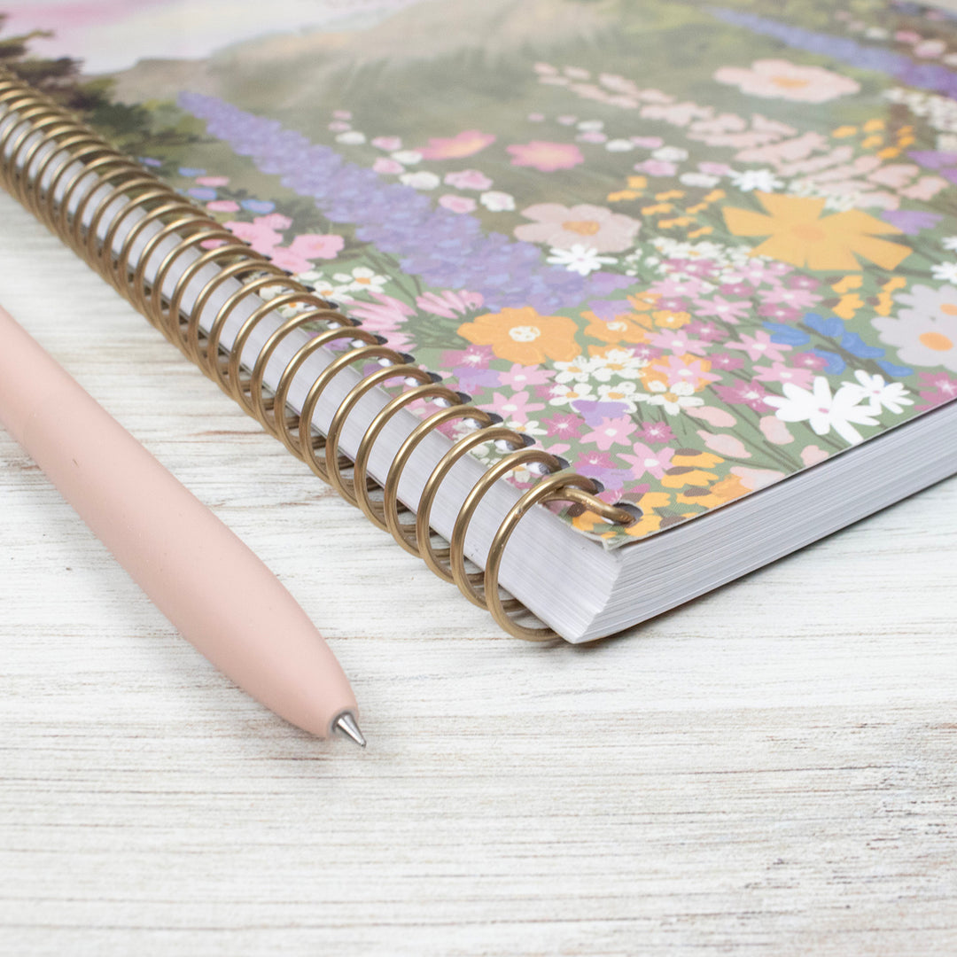 Notebook with floral design on cover and pen on a light wooden surface