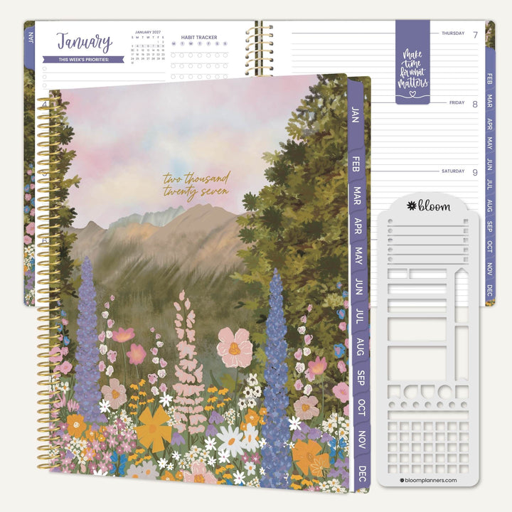 A spiral-bound planner shown open with floral mountain artwork on the cover, interior weekly layout pages, and a white sticker sheet labeled bloom on a clean white background.