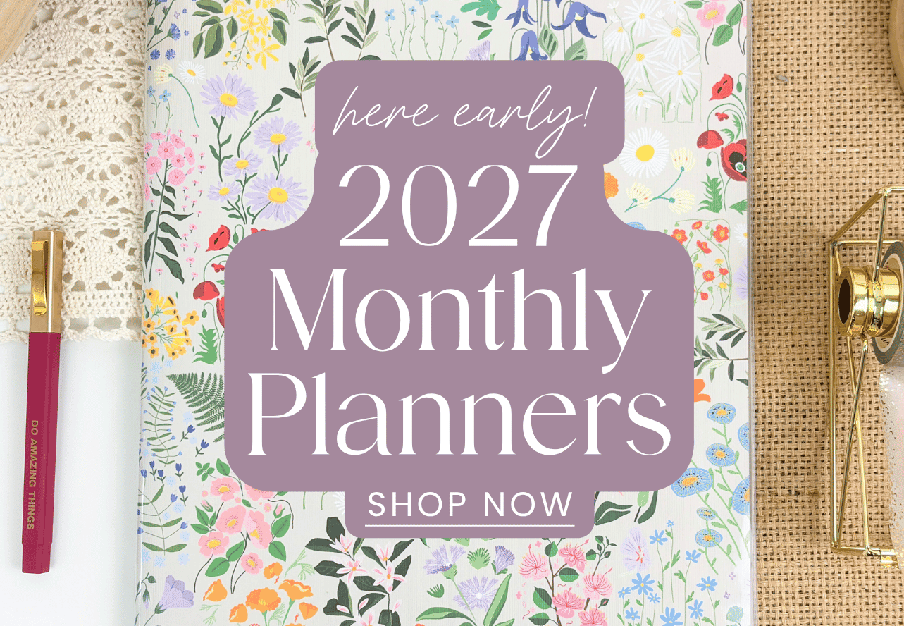 A floral-patterned 2027 Monthly Planner with a large purple 'here early! 2027 Monthly Planners SHOP NOW' badge overlaid in the center. The planner is styled in a flat-lay setting with a gold pen on the left, a lace doily, and a gold hourglass on the right.