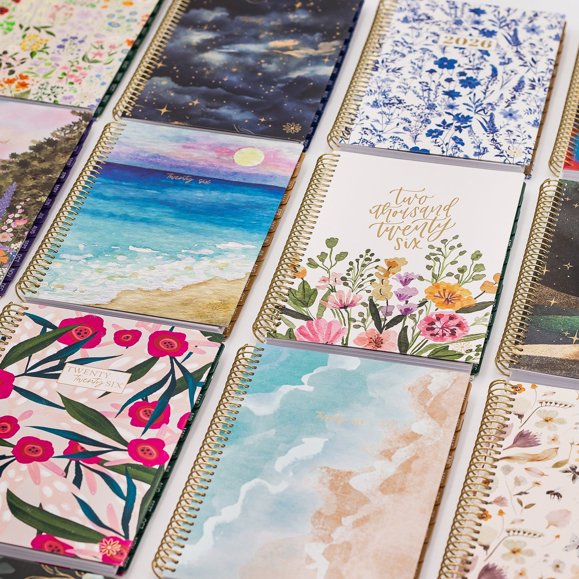 Collection of spiral-bound planners with various designs and text, including '2026' and 'twenty six' gold foil stamps.