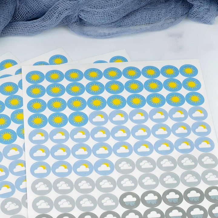 Sheet of weather-themed stickers with sun, cloud, and raindrop symbols on a white background.
