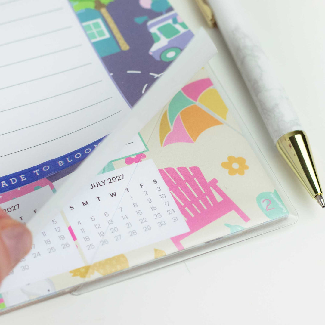 Desk calendar with a colorful design, July 2027 calendar, and a pen on a white surface.