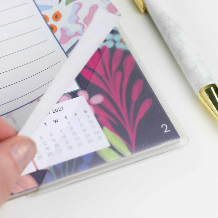 Small calendar with colorful design held by a hand on a white surface.