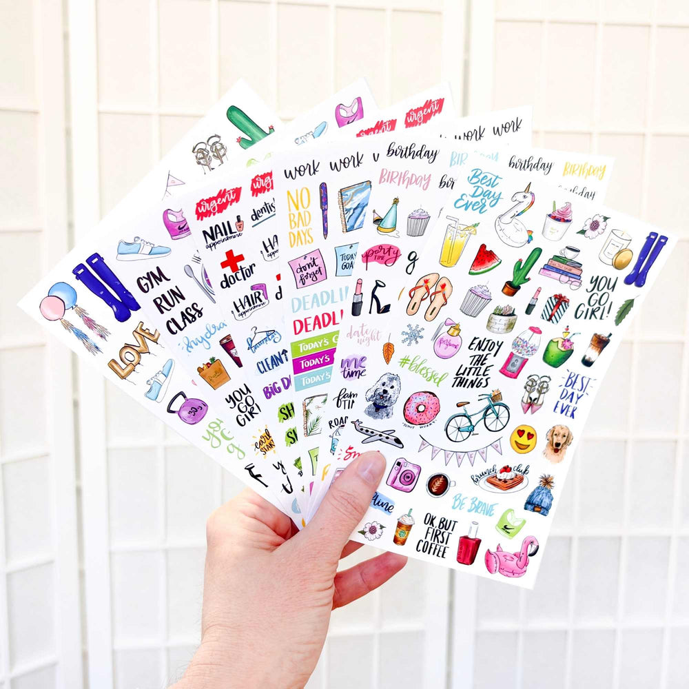 Hand holding a sheet of colorful stickers with various designs on a tiled wall background