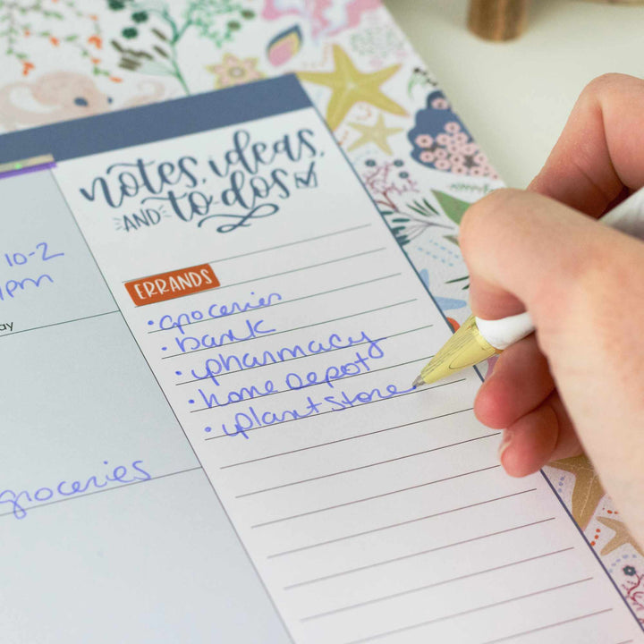 Hand writing on a planner with a pen, surrounded by decorative elements.