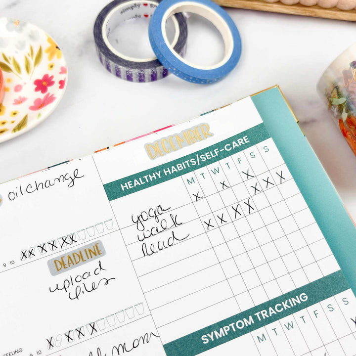 Planner with self-care and habit tracking on a desk with tape and a plate.
