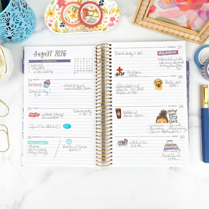 Planner with August 2026 schedule on a white surface with decorative items.