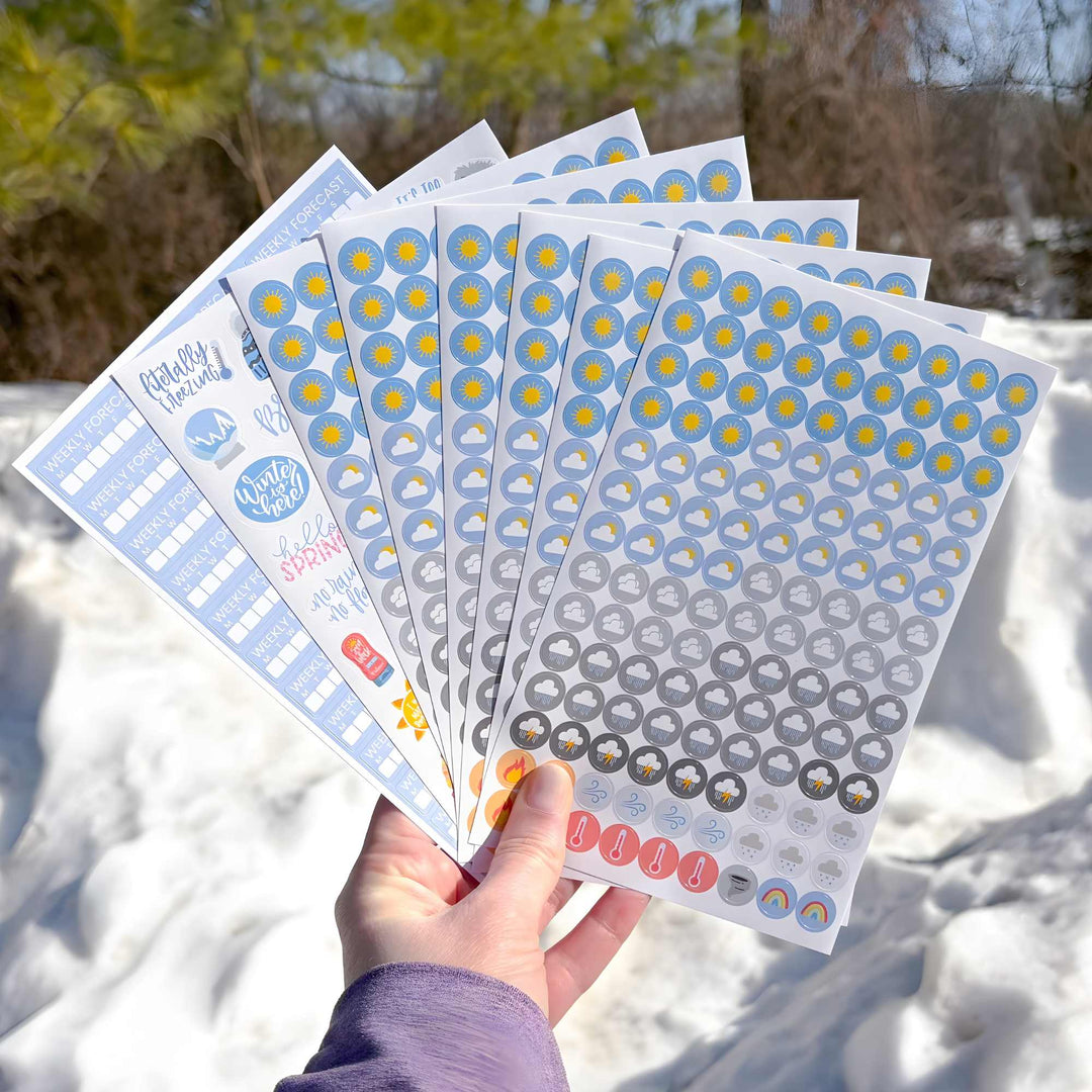 Hand holding sheets of decorative stickers with a snowy background