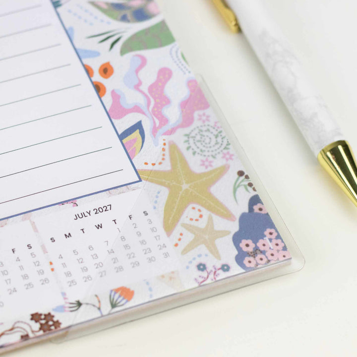 Calendar with floral and starfish design on a white surface with a pen.