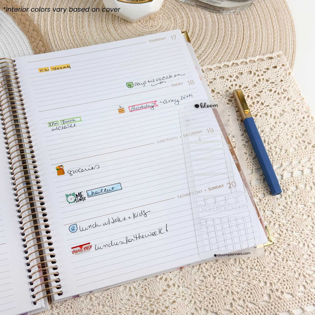 An open spiral-bound planner or notebook spread on a beige lace surface, showing lined pages with handwritten notes and a weekly calendar grid. A blue pen with a gold cap rests to the right, and part of a white cup is visible at the top edge.