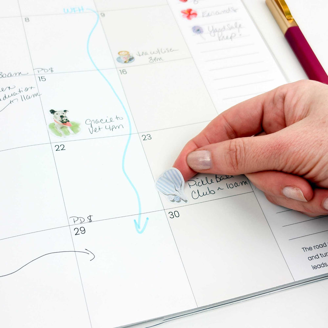 Hand placing a pickleball sticker onto a planner calendar square