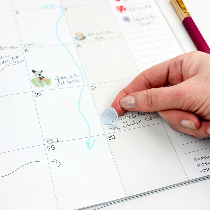 Hand placing a pickleball sticker onto a planner calendar square