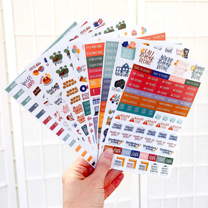 Hand holding sheets of colorful planner stickers with various designs on a white background