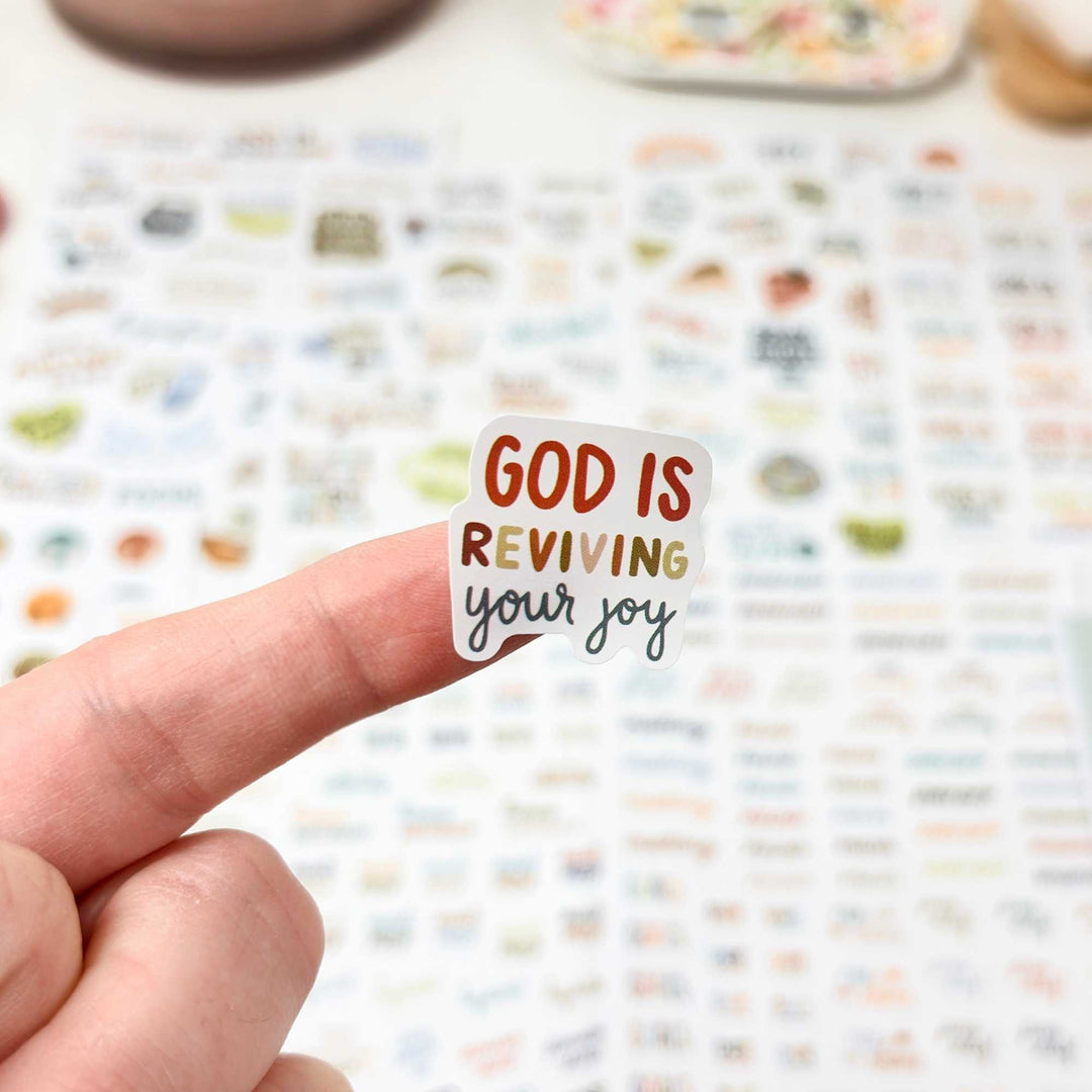 A close up sticker of a finger with a sticker "god is reviving your joy" on it 
