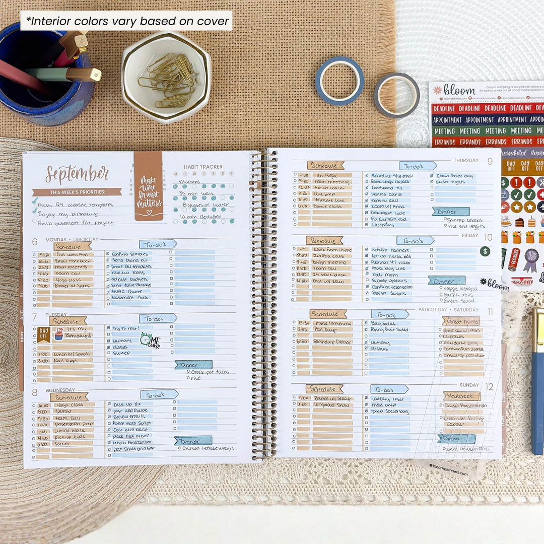 An open spiral-bound planner shown from above on a burlap surface, with printed weekly and monthly layouts, stickers, washi tape, a pen cup, and a blue pen around it. The top-left text says interior colors vary based on cover.