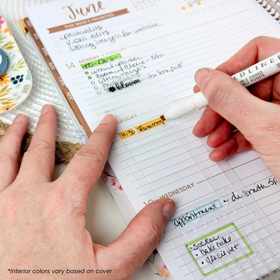 A close-up of a person's hands writing in a weekly planner page with a white pen. The planner has a white grid layout with columns for Monday through Sunday and a weekly schedule box.