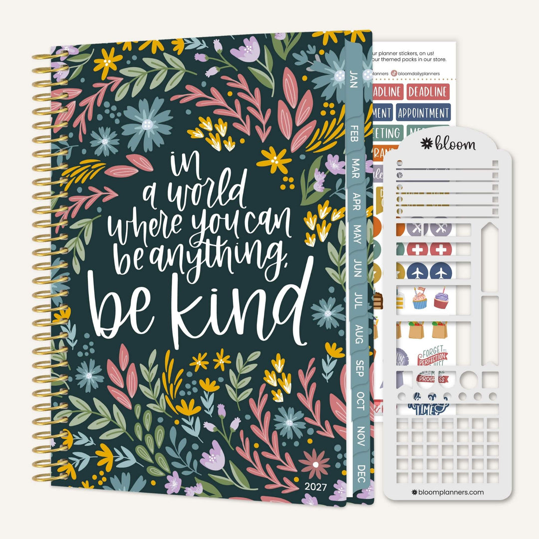 A floral planner set shown on a light neutral background, featuring a spiral-bound 2027 planner with a dark teal cover covered in multicolored flowers and the phrase 'in a world where you can be anything. be kind.